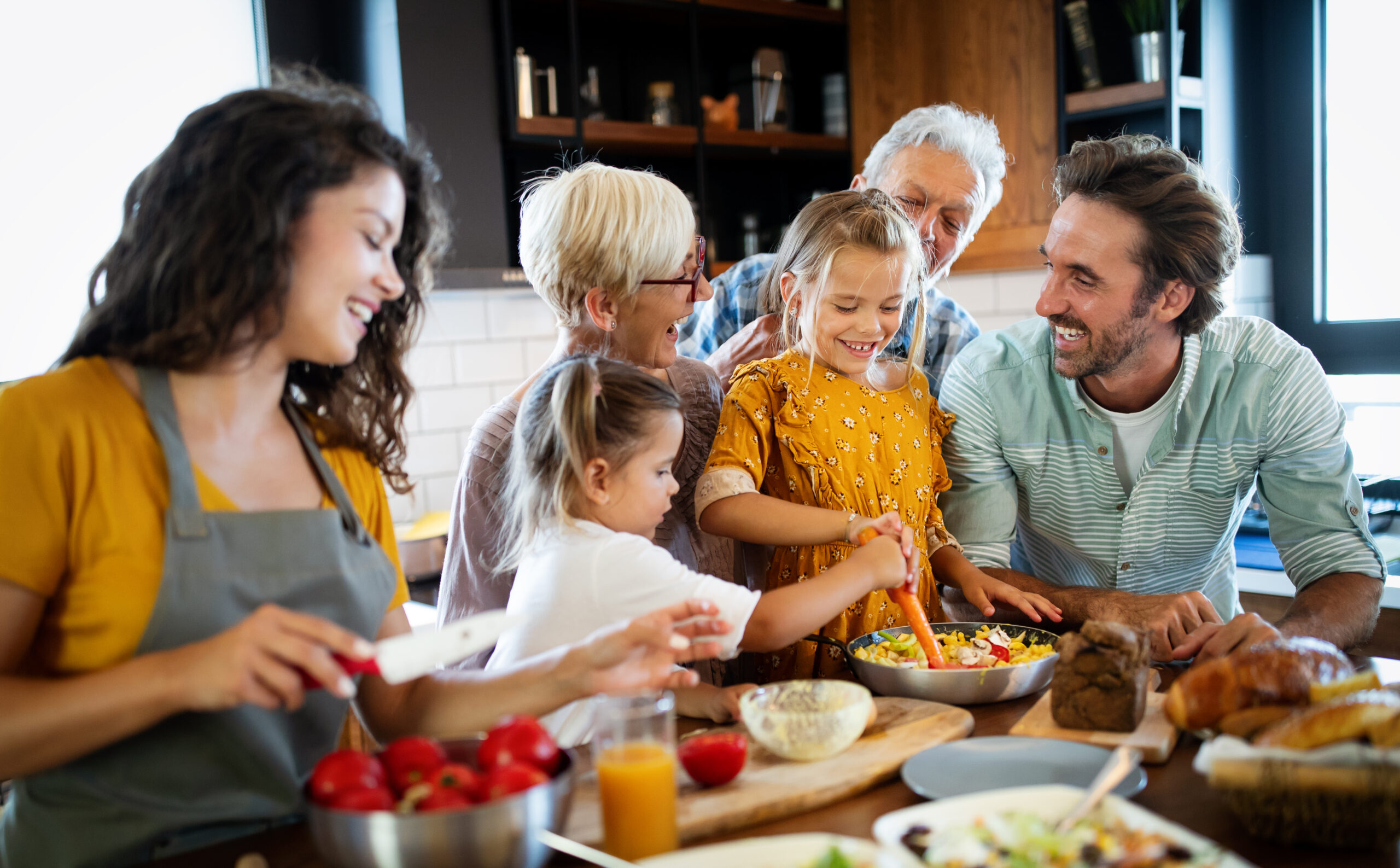 Picture of a family cooking together in the kitchen, with various international ingredients and dishes laid out on the counter