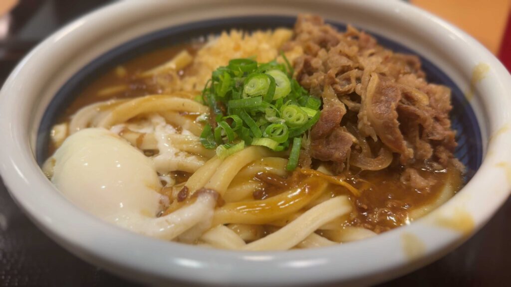 Curry nikutama udon topped with beef, green onions, tempura flakes, and a soft-cooked egg at Marugame Udon in Waikiki.