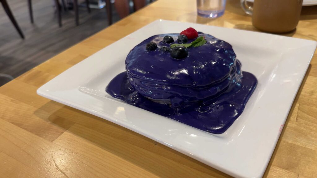Stack of ube pancakes covered in purple sauce and topped with blueberries, a raspberry, and mint at Yogur Story in Honolulu.