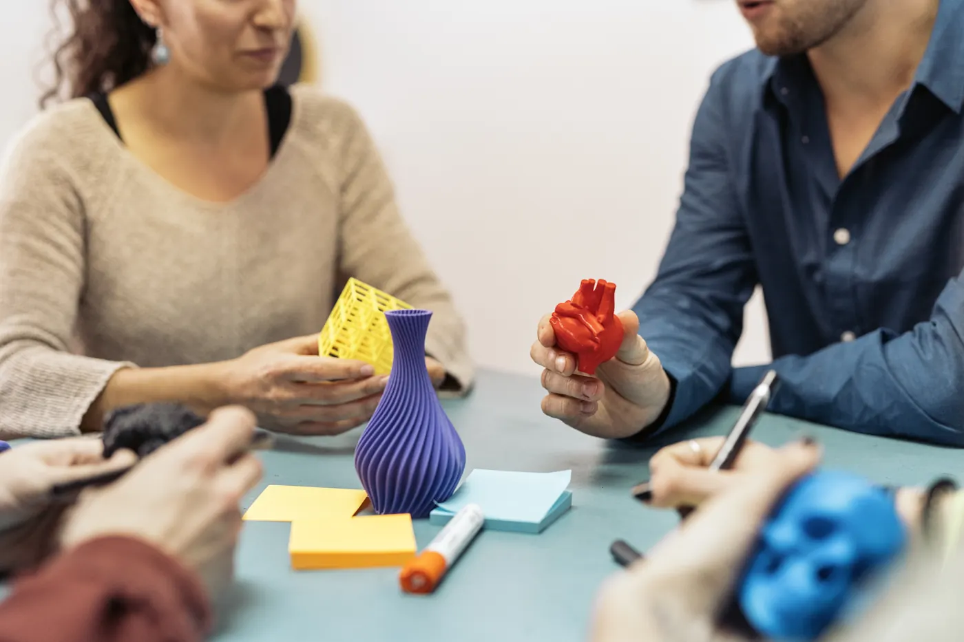 People at a table hold colorful printed objects beside a purple decorative model and project notes.