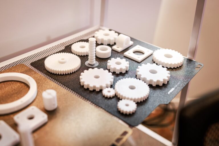 White 3D-printed plastic gears and mechanical parts arranged on a printer bed.
