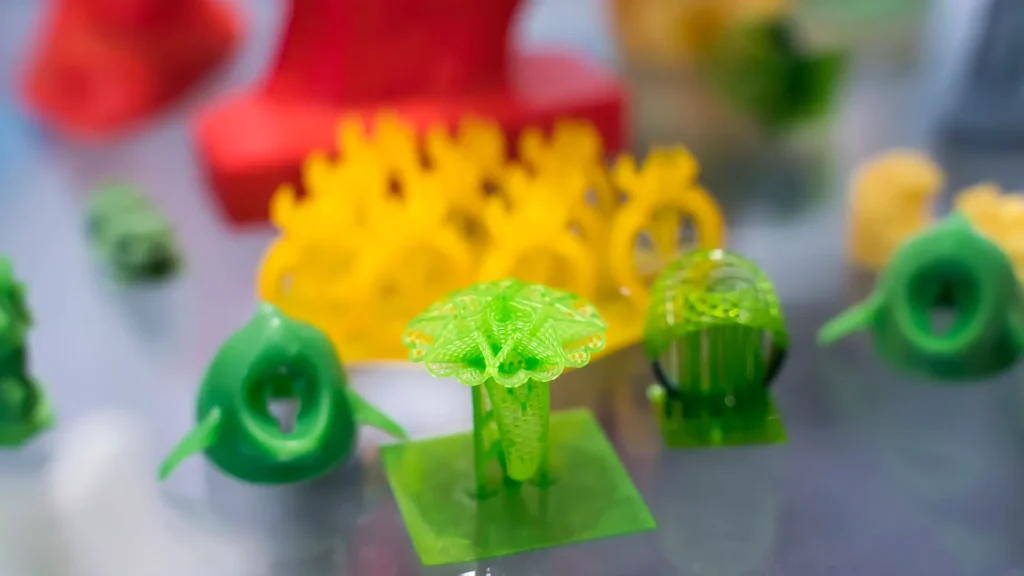 Green branching 3D printed forms and yellow gear-like pieces displayed with other colorful objects