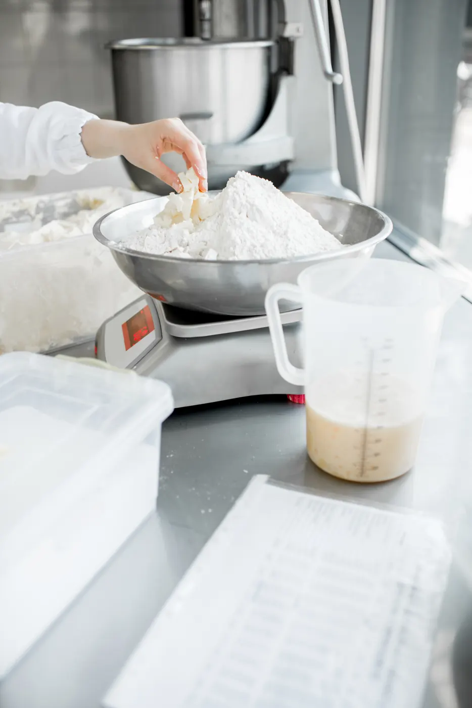 A bowl of flour on a kitchen scale beside a measuring jug and baking equipment.