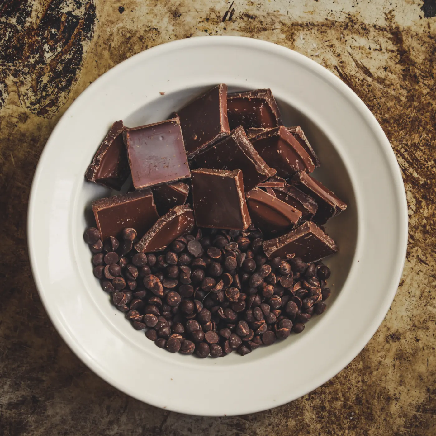 Pieces of a chocolate bar and small chocolate chips arranged in a white bowl