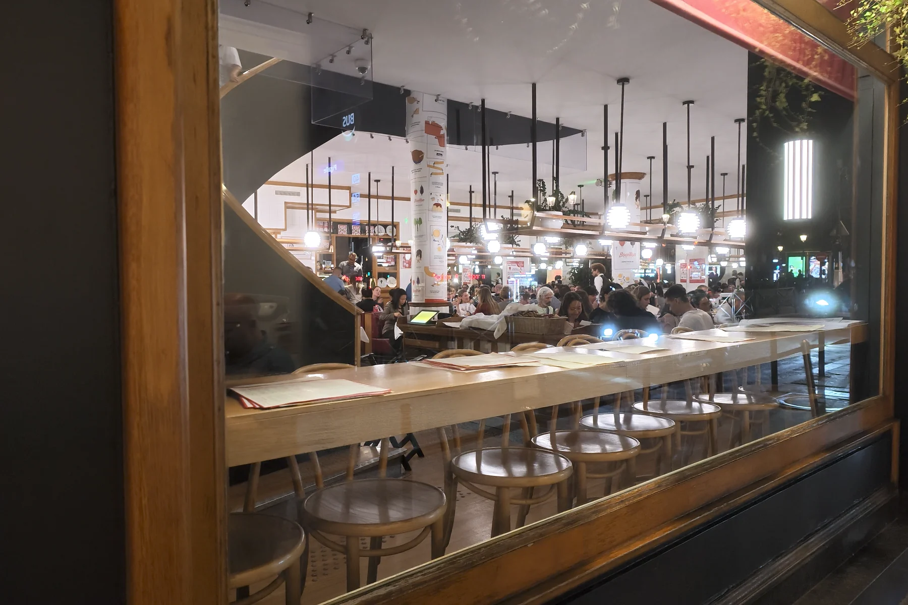 Wooden stools and a window counter overlook the busy, pendant-lit dining room at Bouillon Pigalle in Paris.
