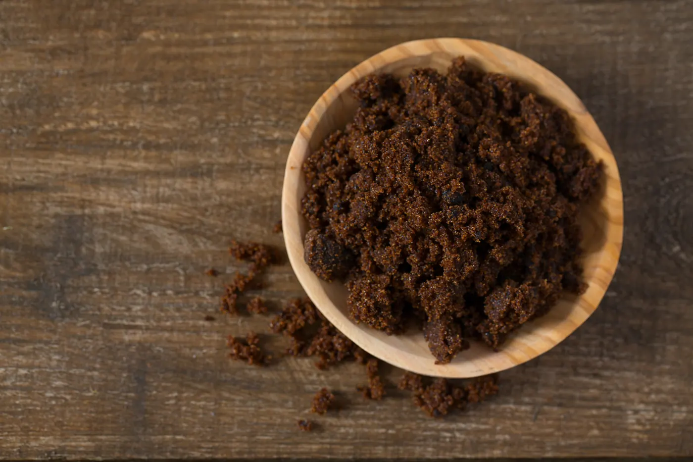 Dark-colored brown sugar in a wooden bowl on a rustic table
