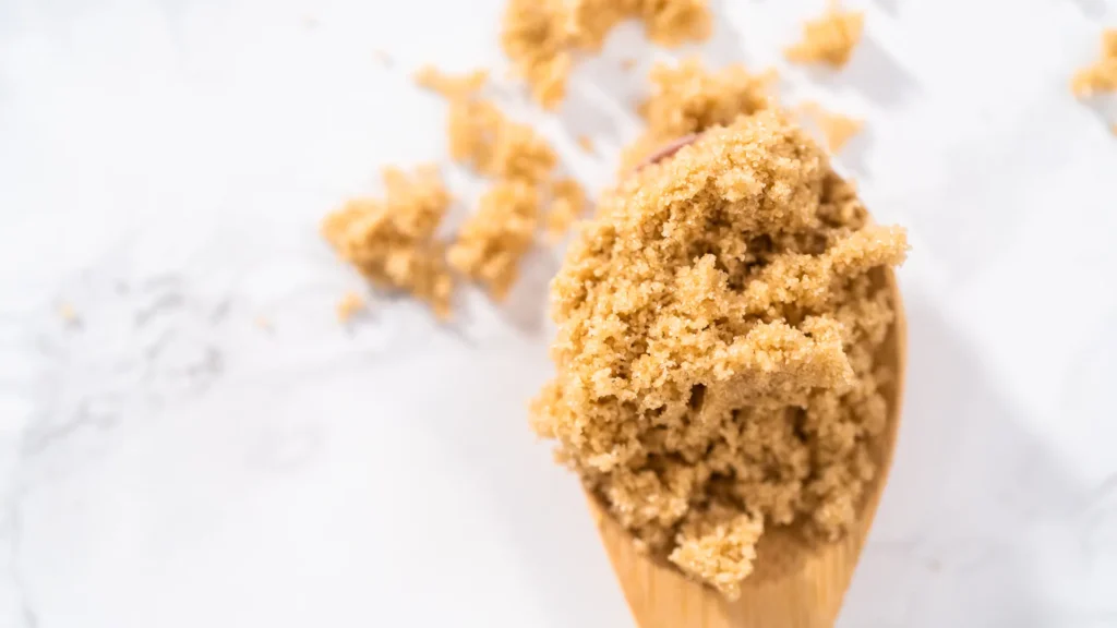 Soft brown sugar piled on a wooden spoon over a pale work surface