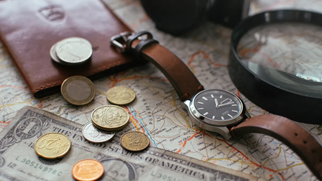 A wristwatch, coins, and a magnifying glass rest on a travel map.