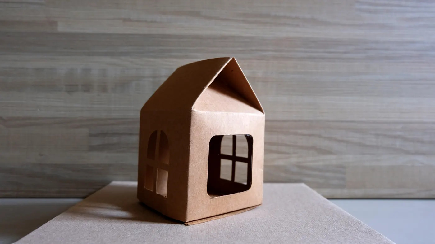 A small brown cardboard house model standing on a neutral surface.