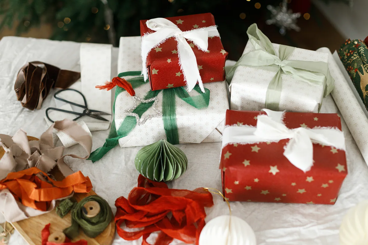 Wrapped Christmas gifts with ribbon, string, and scissors on a fabric-covered work surface.