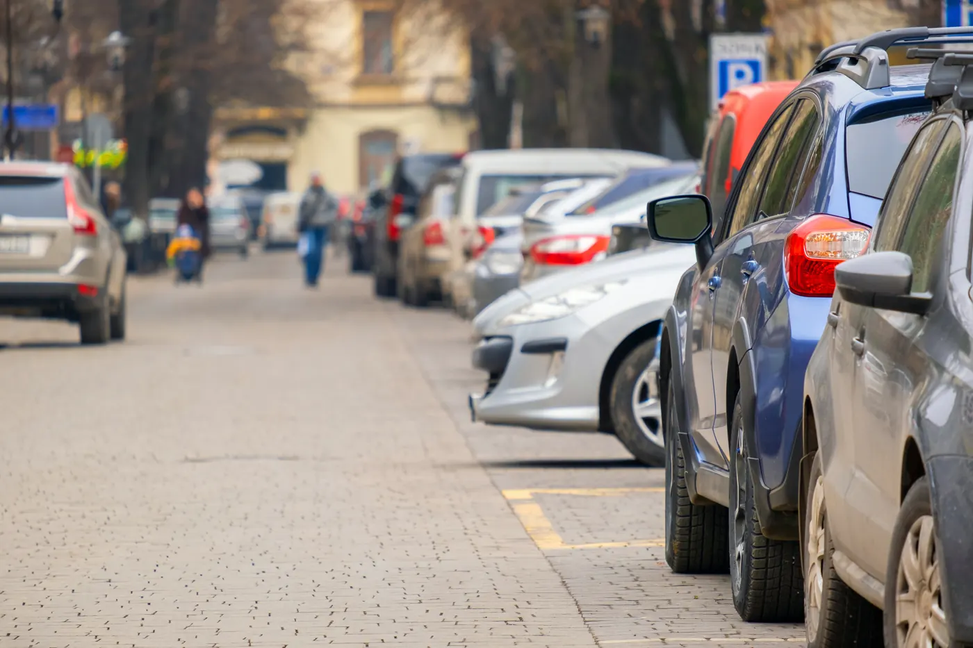 A row of cars parked beside a cobblestone city street.