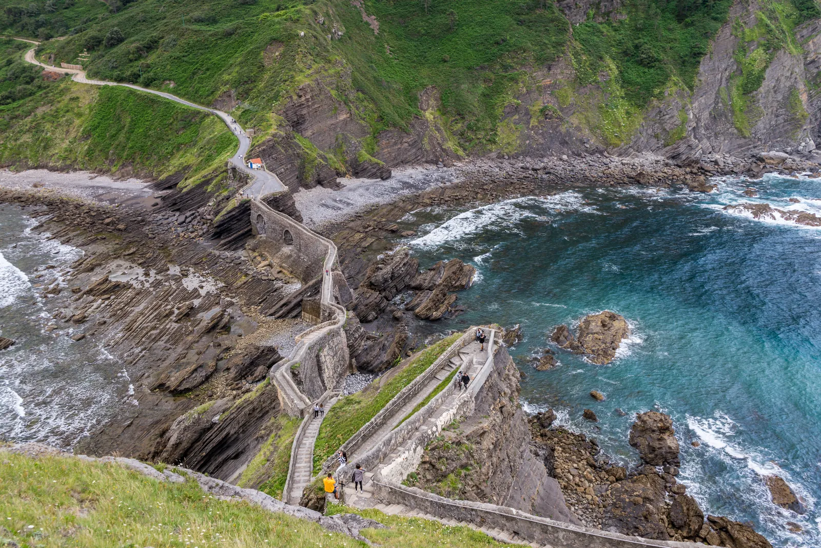 A winding stone walkway crosses a rocky green coastline above blue ocean water.