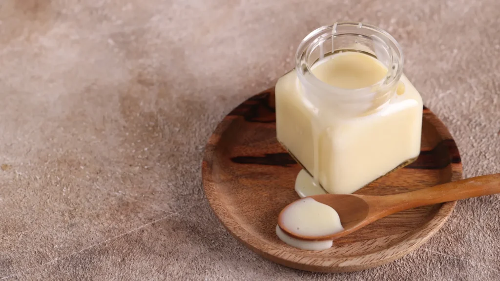 Glass jar of condensed milk and a wooden spoon on a round wooden board