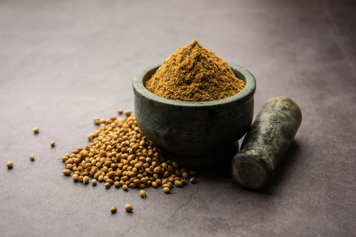 Whole coriander seeds beside ground coriander in a stone mortar.