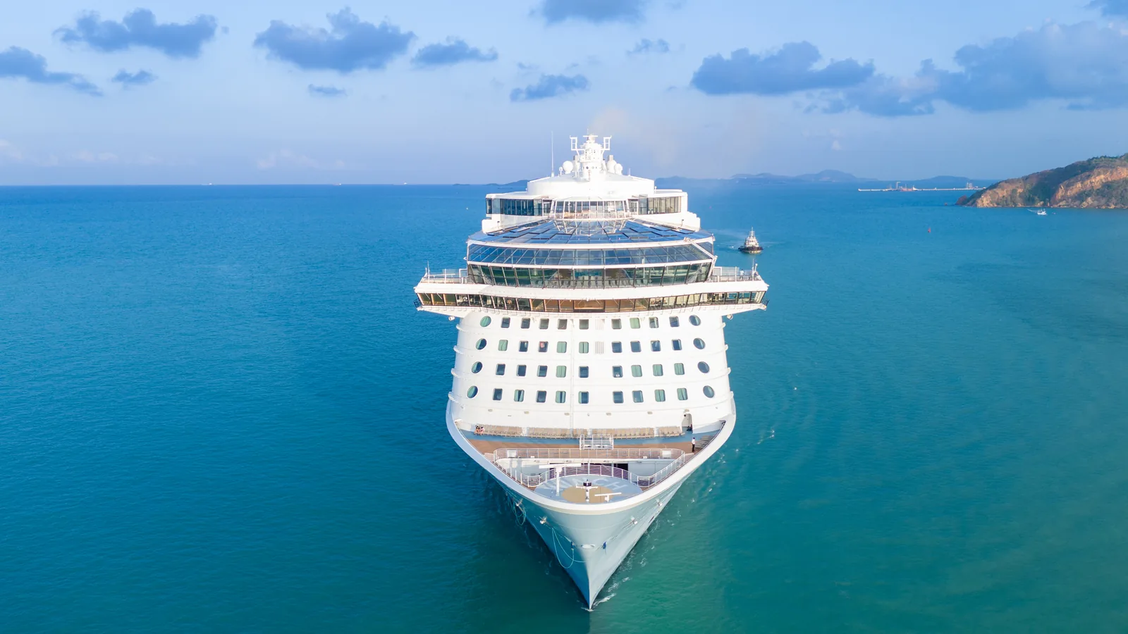A large cruise ship viewed from the bow while anchored in blue ocean water near islands.