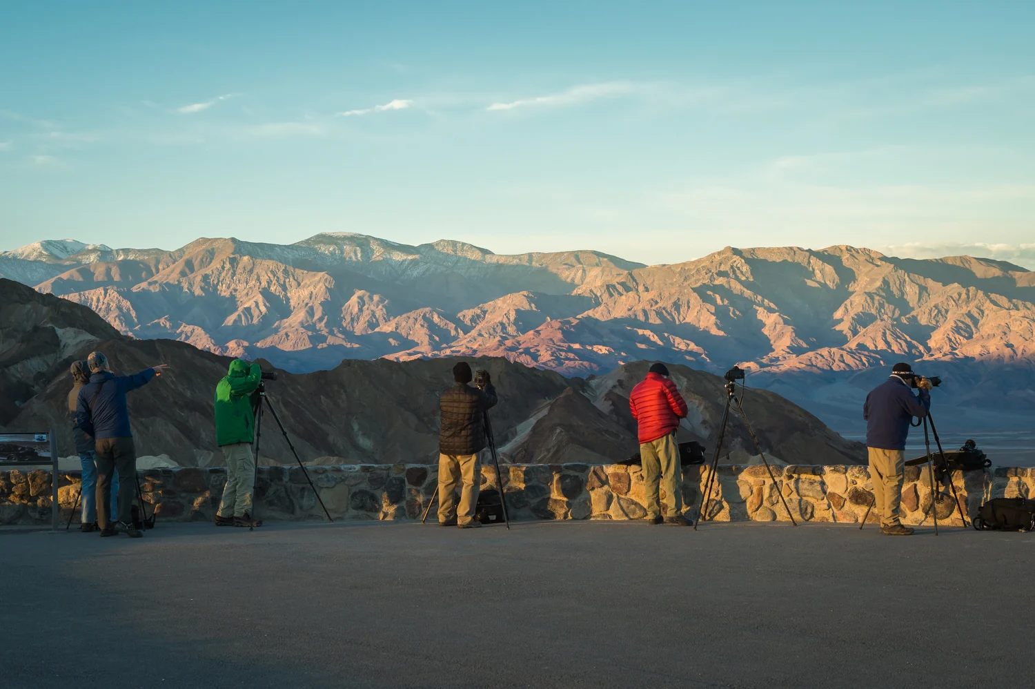 Visitors looking out from the Zabriskie Point terrace toward sunlit badlands.