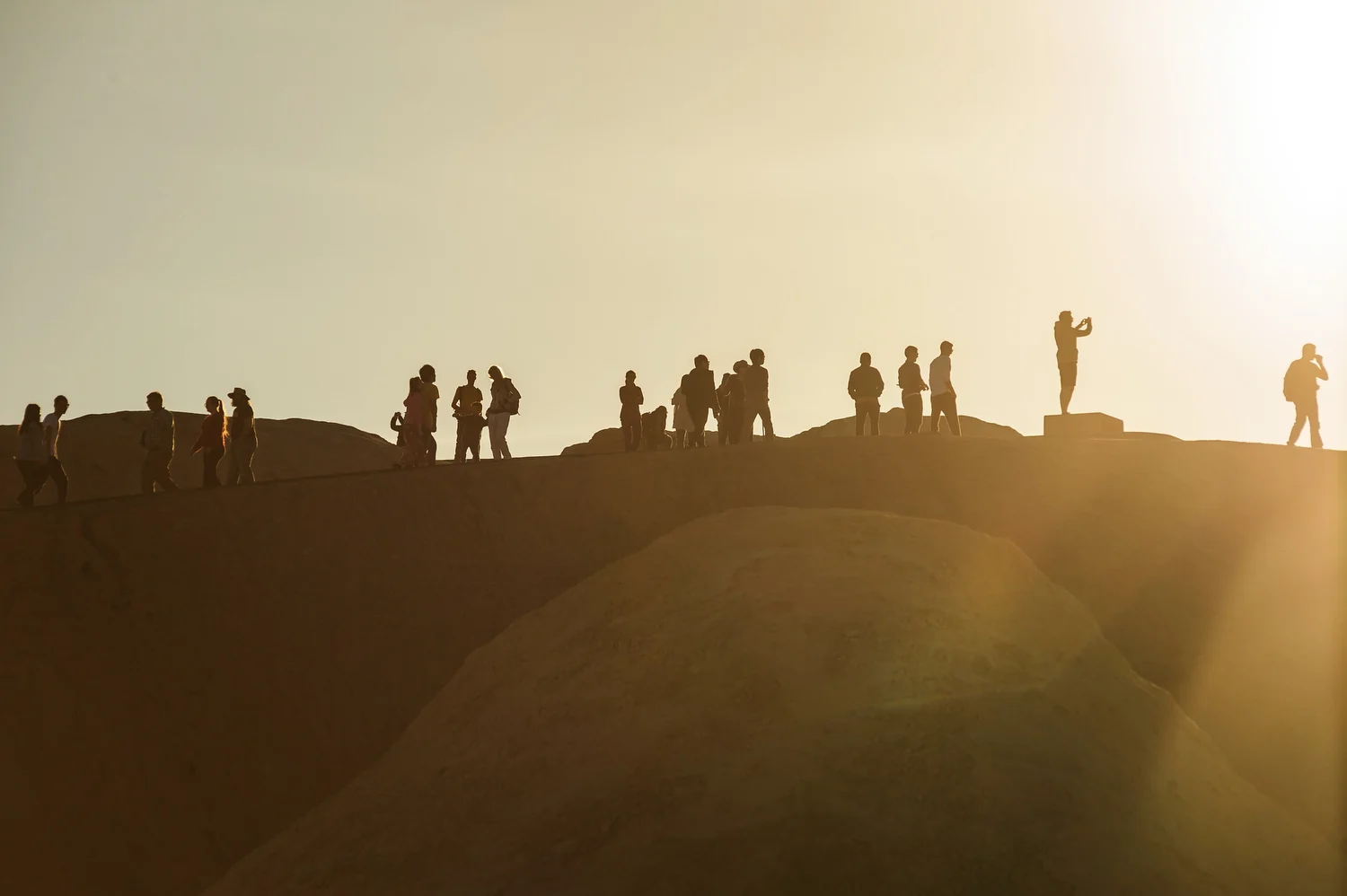 Visitors silhouetted at Zabriskie Point as the sun approaches the horizon.