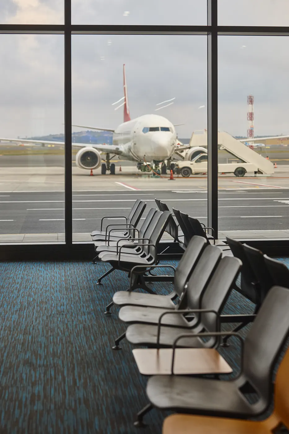 Rows of empty airport seats face a parked airplane through tall terminal windows.