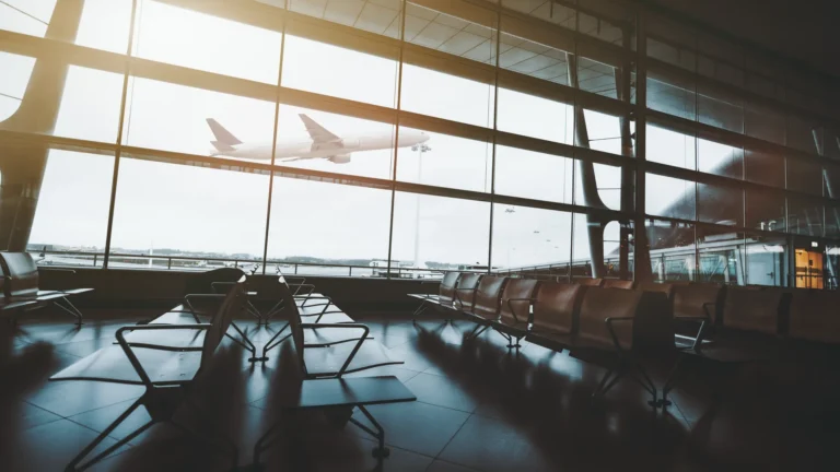 An airplane takes off beyond the windows of an empty airport waiting area.