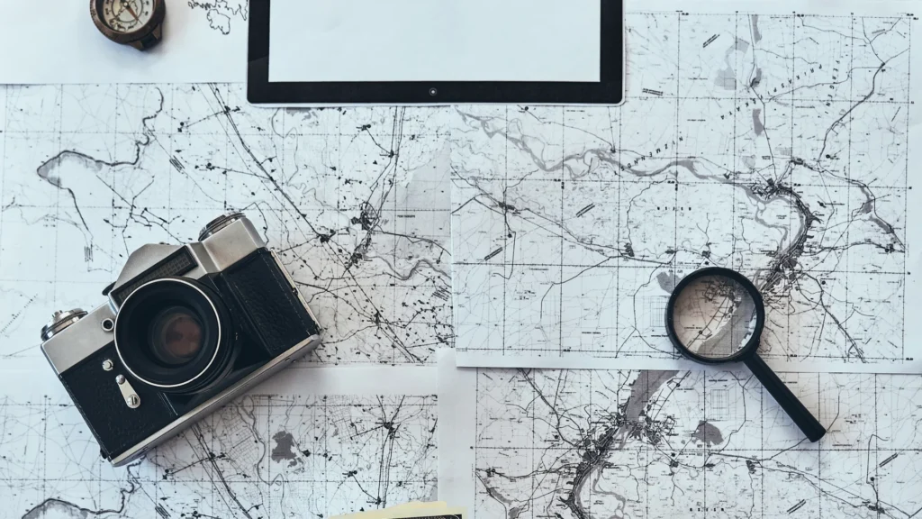 A travel map with a camera, compass, and smartphone arranged for planning.