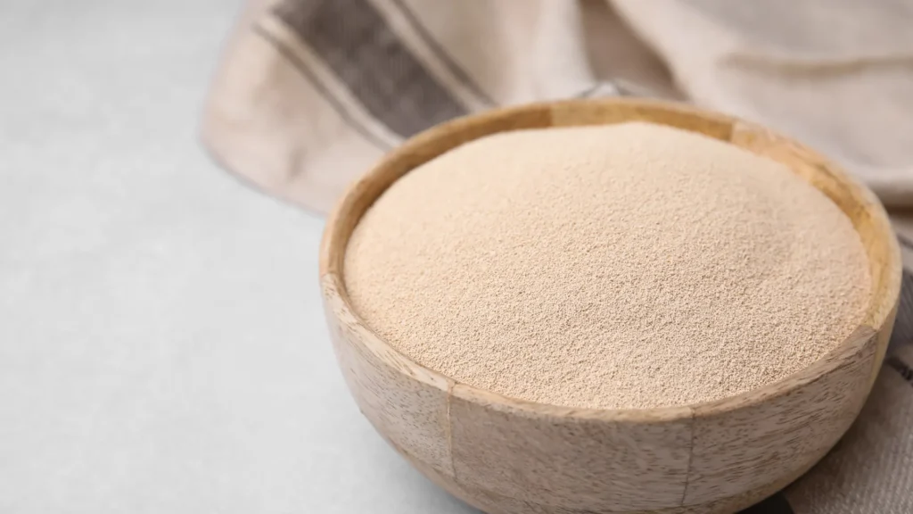 Fine dry yeast granules in a wooden bowl on a pale counter beside a cloth