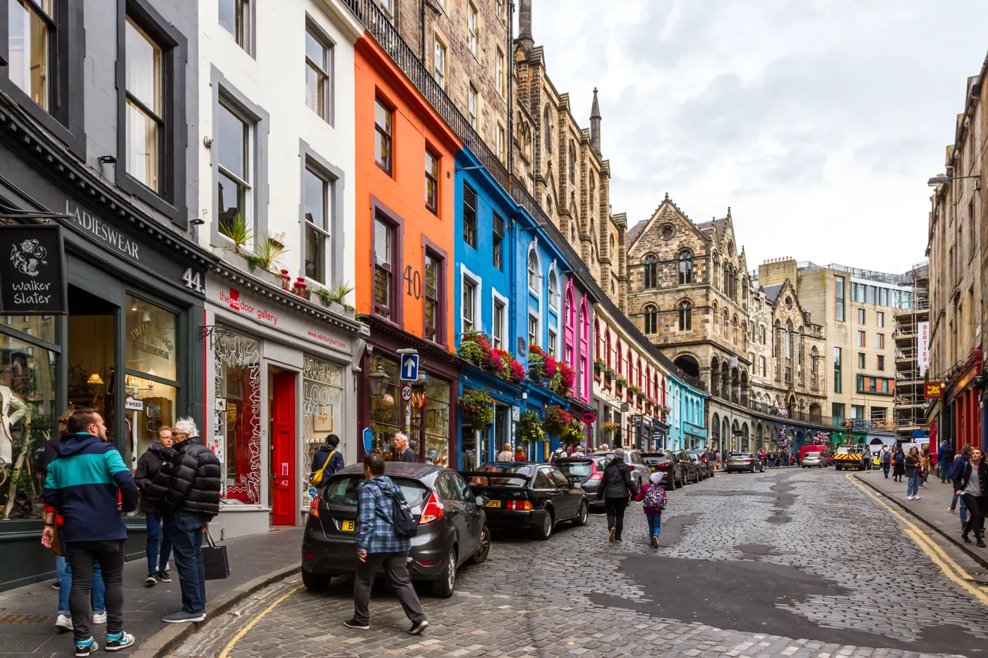 Colorful shopfronts and pedestrians along a cobbled street in Edinburgh Old Town