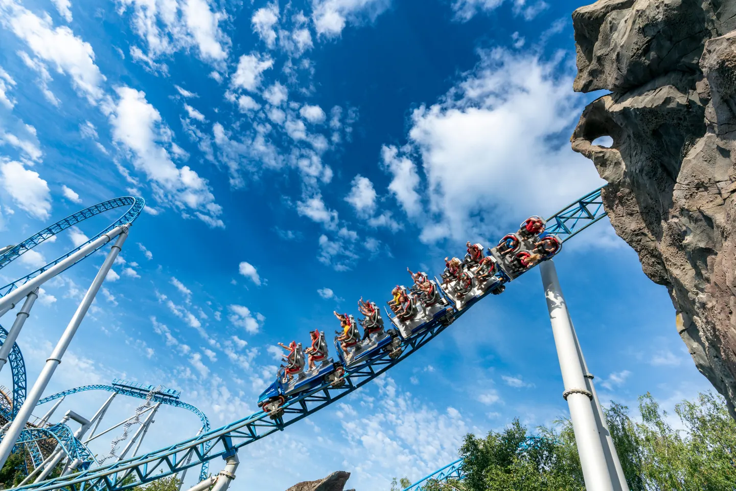 A blue fire coaster train sweeping along blue track beneath a clear sky.