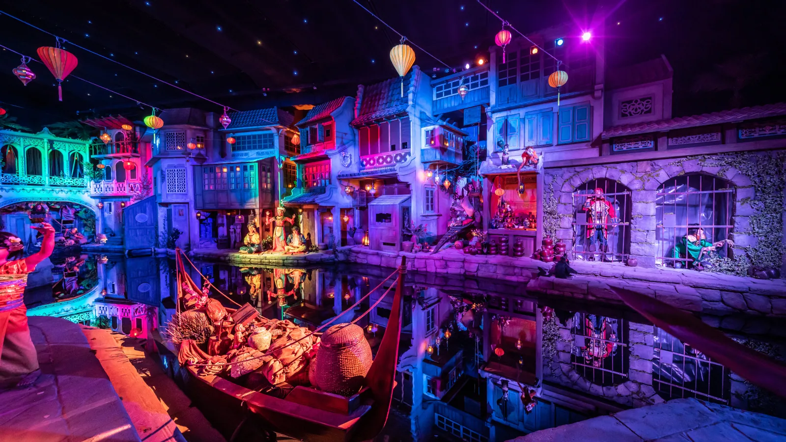 A boat passing illuminated harbor scenery inside Pirates in Batavia.