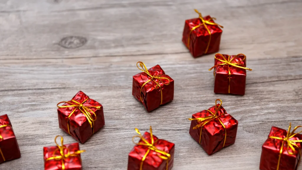 Small red decorative gift boxes tied with gold ribbon on a gray wooden surface.