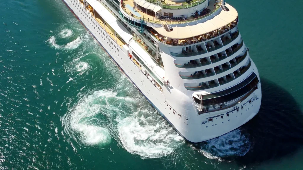 An aerial view of a cruise ship bow moving through turquoise water.