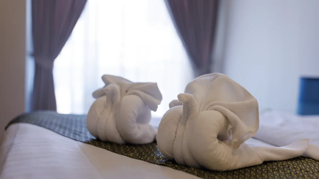 Two white towels folded into elephant shapes on a hotel bed.