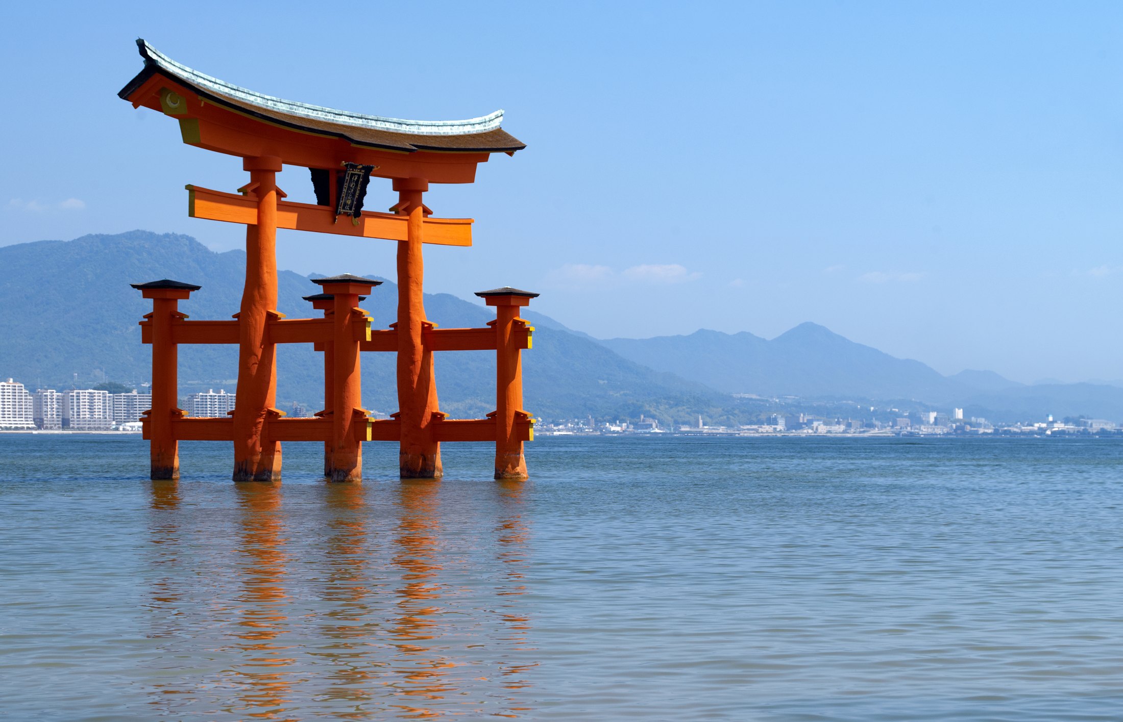 Itsukushima Shrine’s vermilion torii stands in the sea off Miyajima with hills behind it