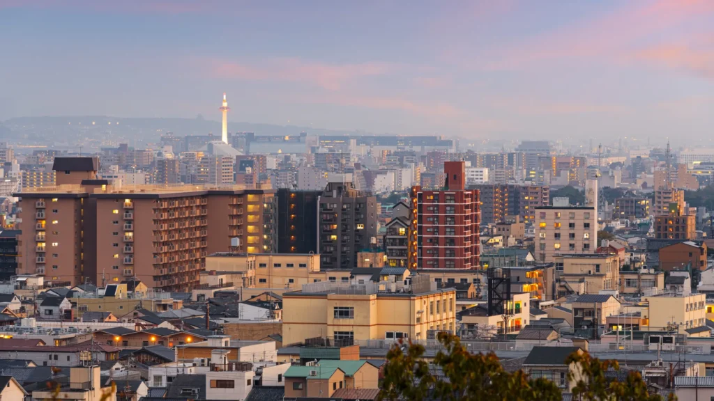 Kyoto city buildings at dusk beneath a pink sky, with Kyoto Tower illuminated in the distance
