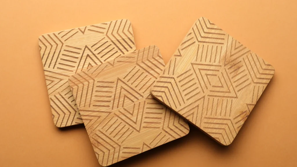 Three square wooden coasters display engraved geometric line patterns on a tan background.