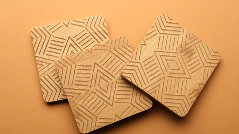 Three square wooden coasters display engraved geometric line patterns on a tan background.
