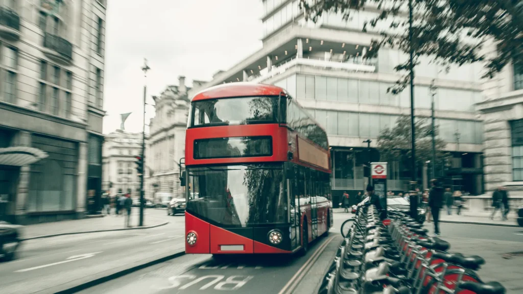 A red double-decker bus moves along a London street beside a row of bicycles.