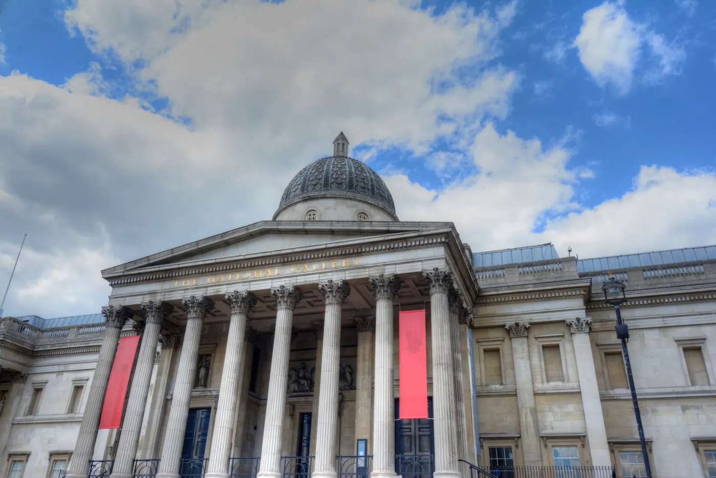 The National Gallery's columns and dome rise beneath a blue, clouded sky in London.
