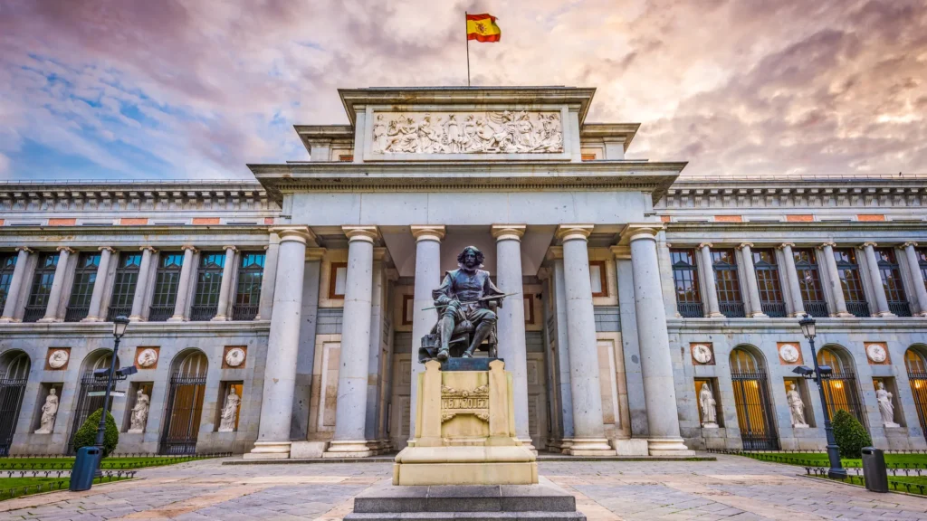 Prado Museum facade and Velázquez statue beneath a colorful evening sky in Madrid