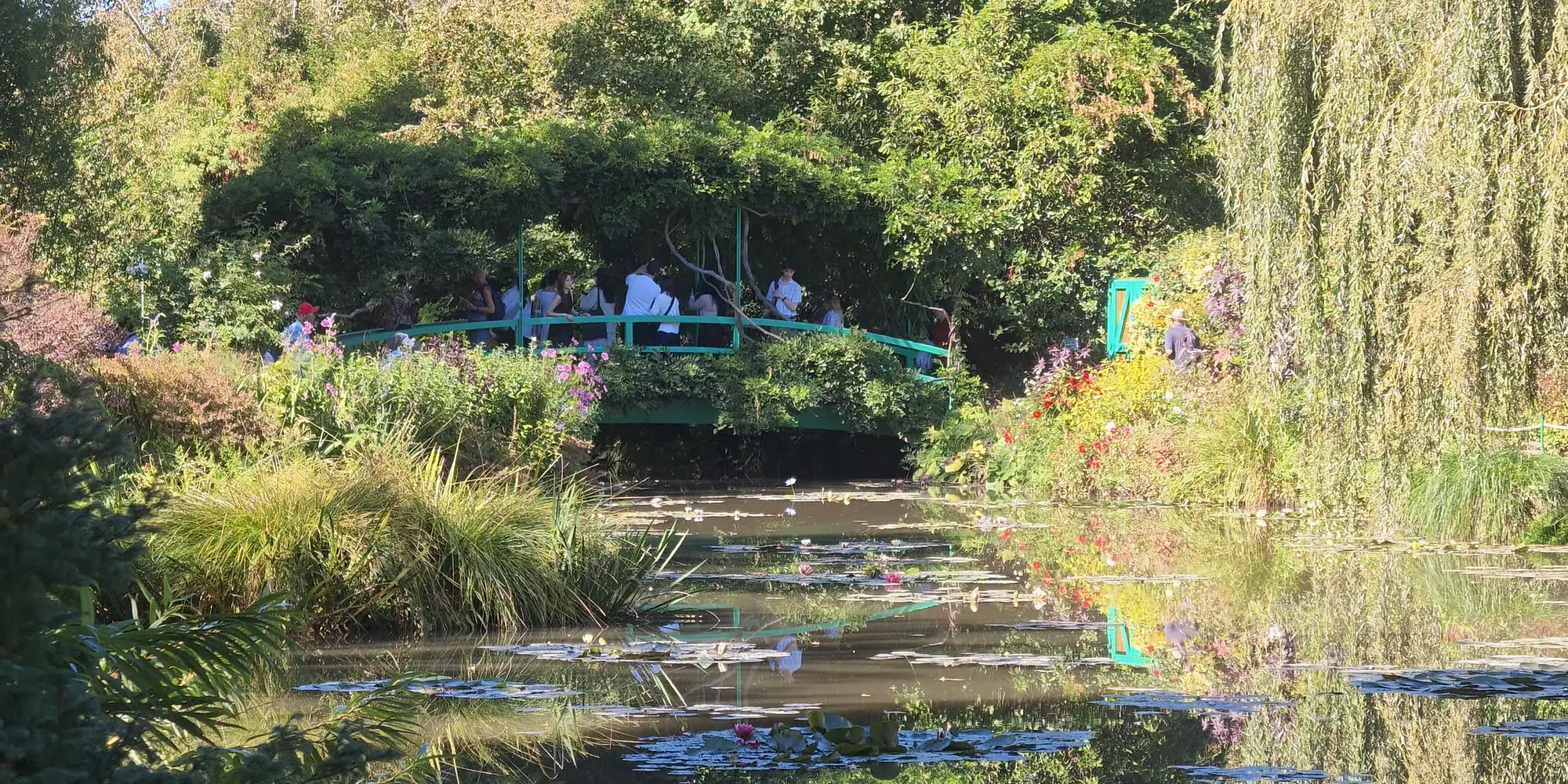 The green Japanese bridge spans Monet’s water garden in Giverny, surrounded by foliage and reflections.