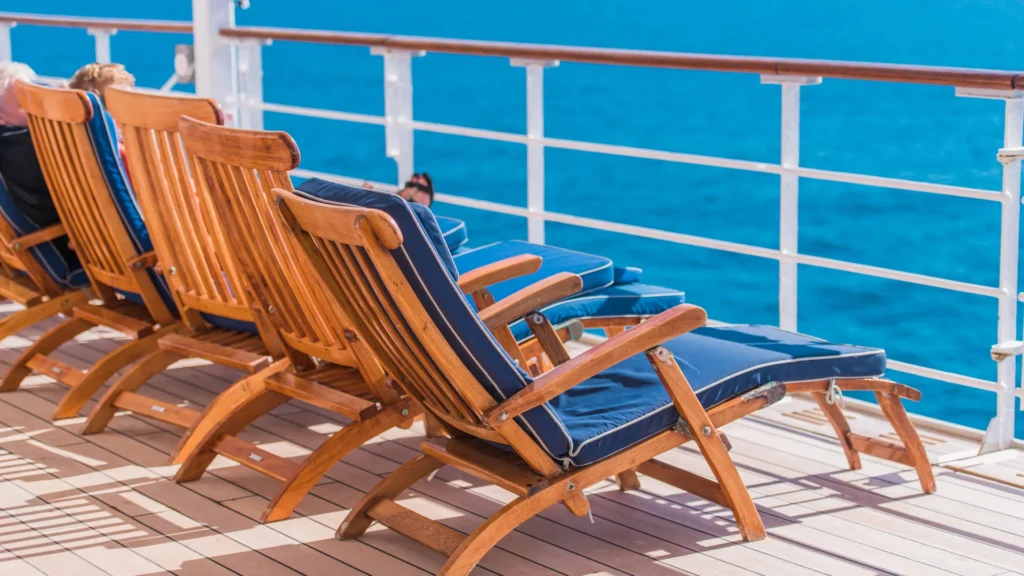 Wooden lounge chairs face blue water from a ship deck.