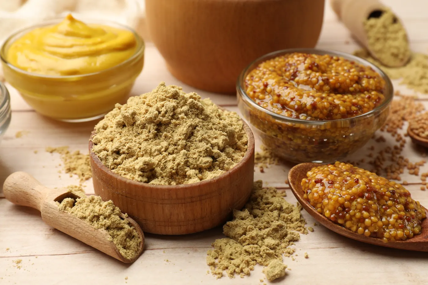 Ground mustard powder in a wooden bowl beside smooth and grainy prepared mustards.
