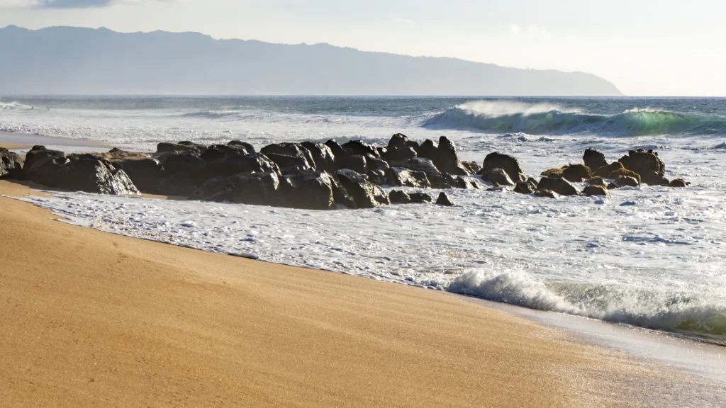 Waves meet a sandy beach and rocks on the North Shore of Oahu.