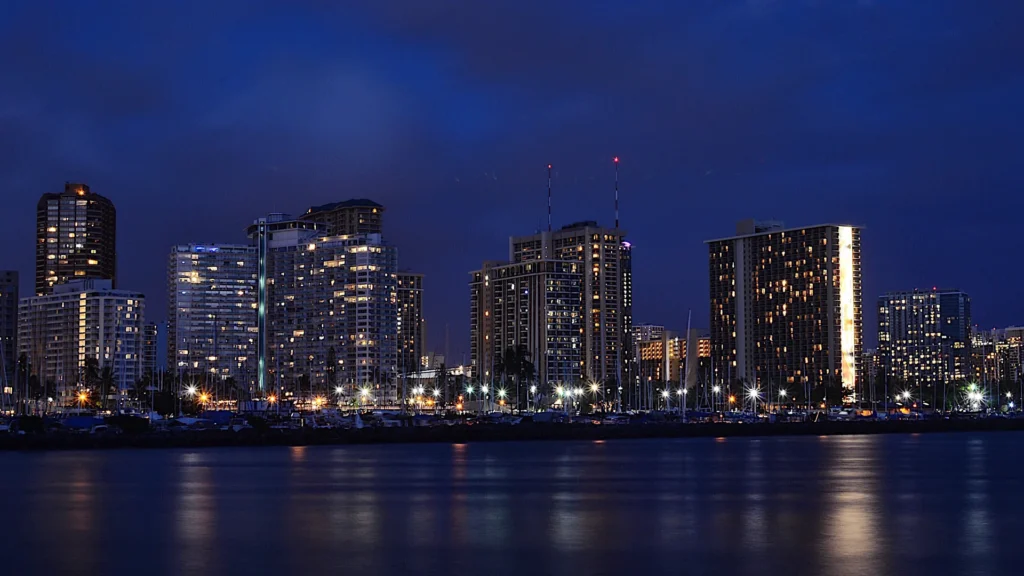 Illuminated Waikiki buildings reflected in the water at night.