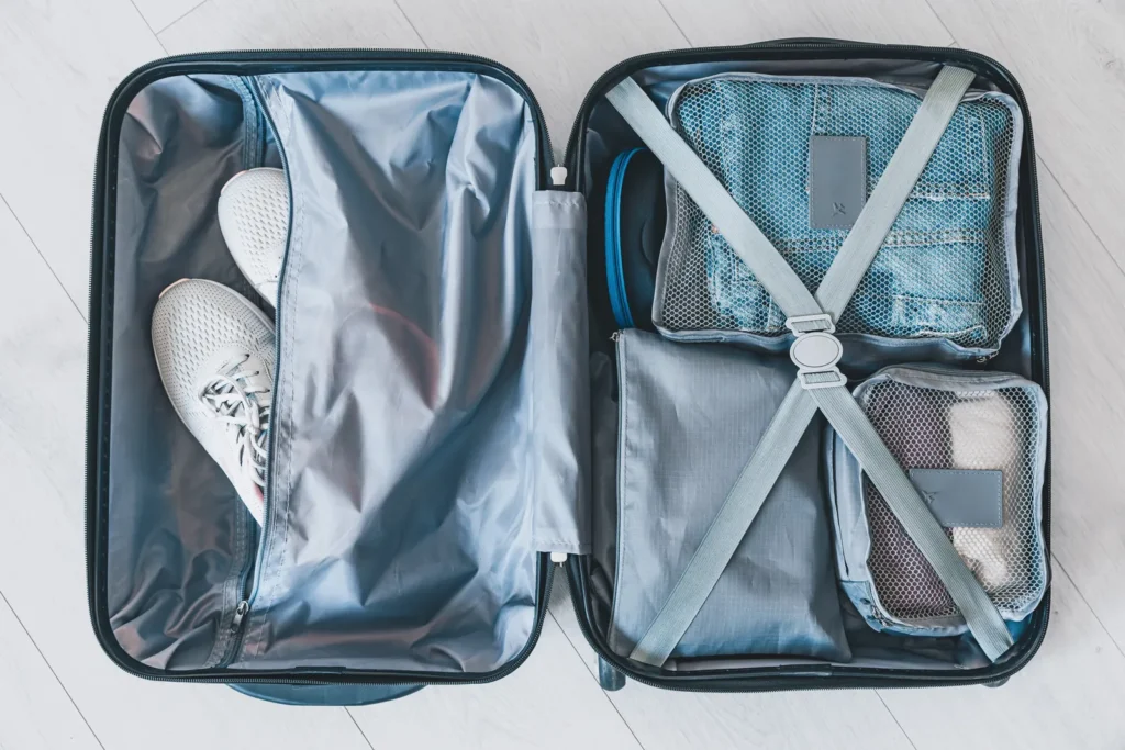 An open gray suitcase with mesh packing cubes, clothing, and white sneakers.
