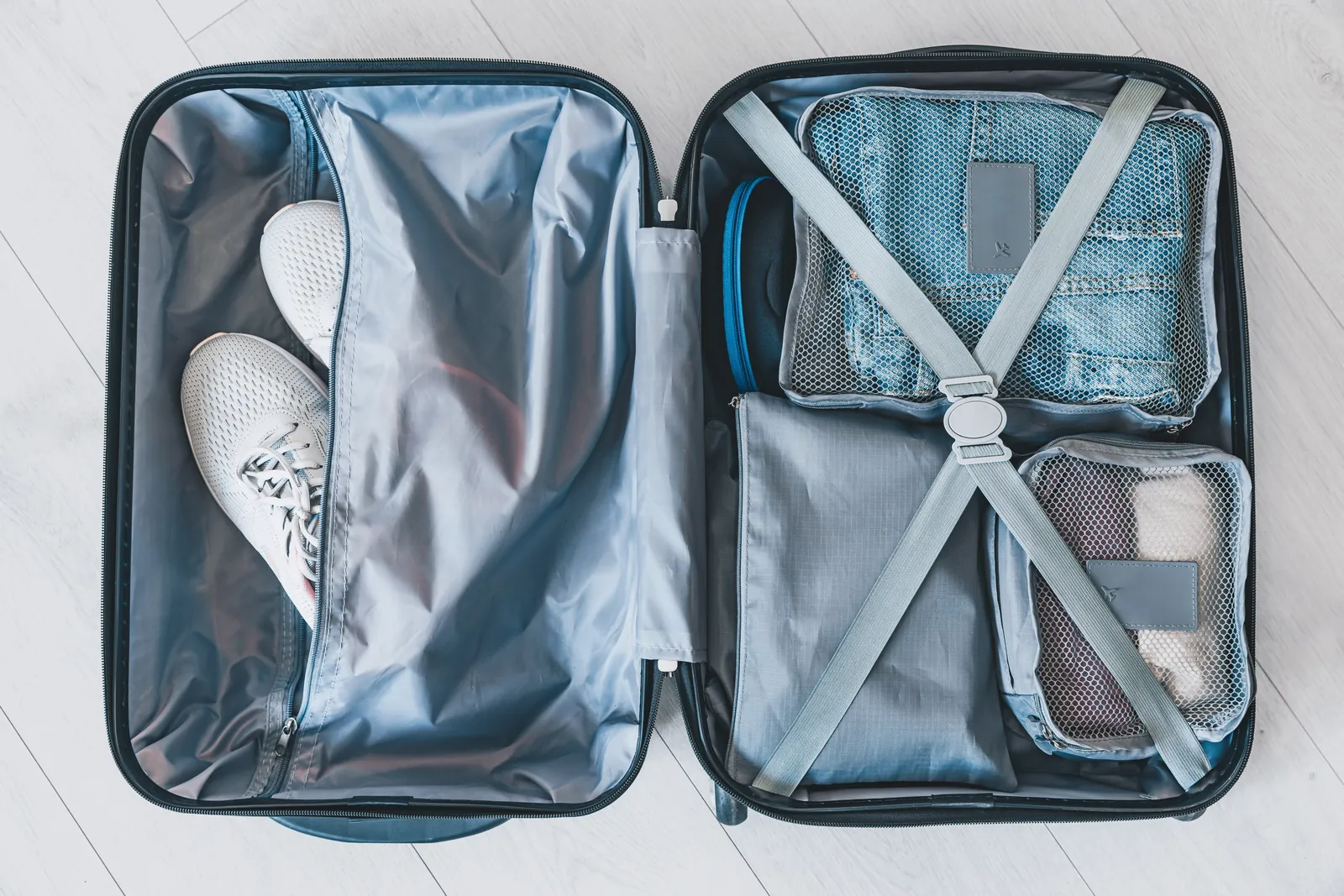 An open gray suitcase with mesh packing cubes, clothing, and white sneakers.