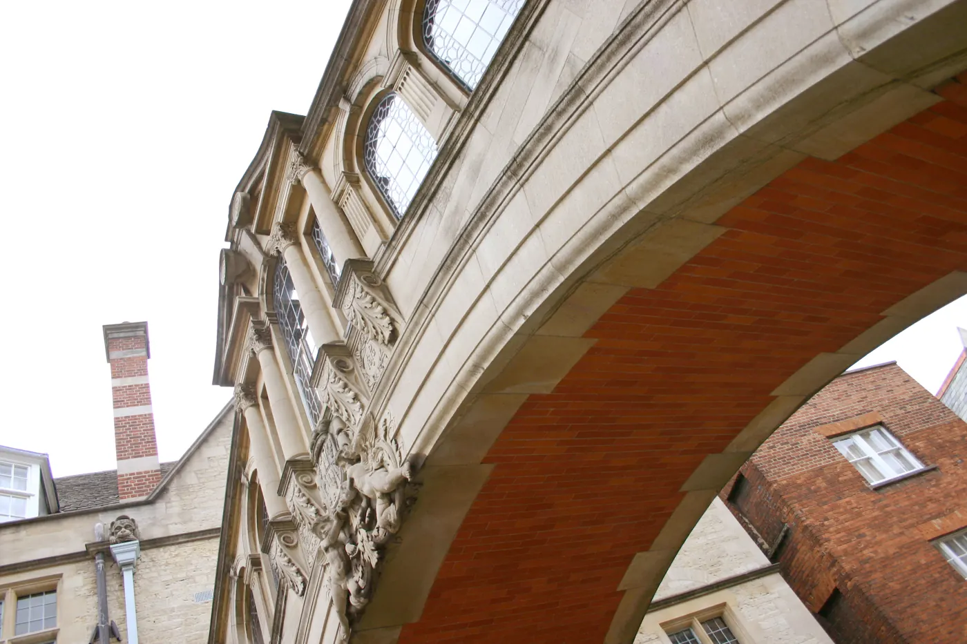 Low-angle view beneath an enclosed stone bridge between buildings in Oxford