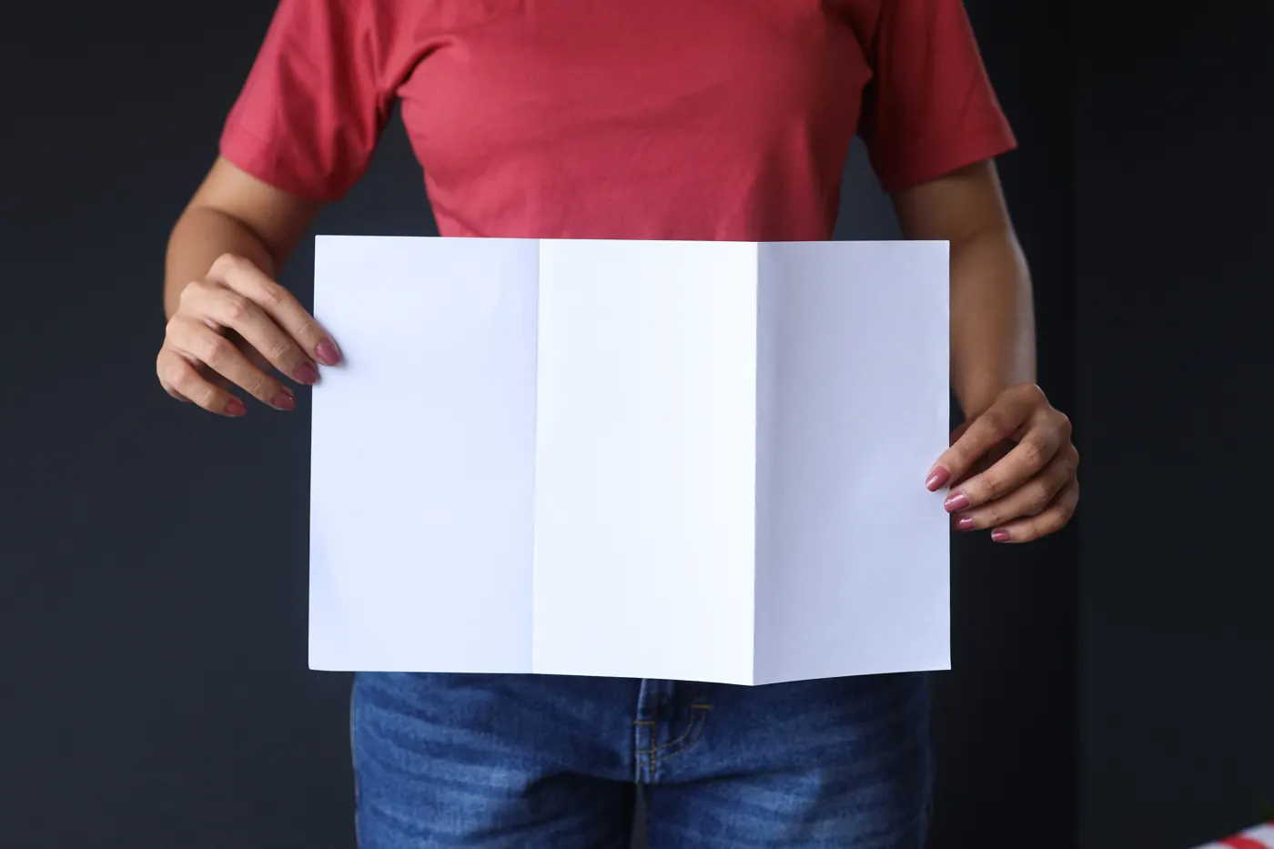 A person in a red shirt holding open a blank white sheet with two vertical folds
