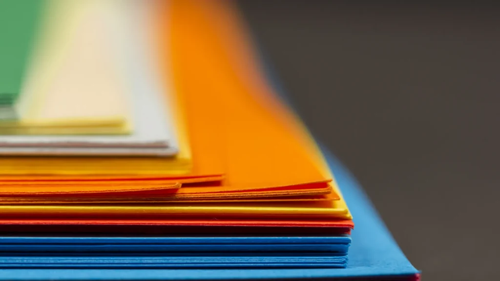 Layered sheets of blue, orange, green, and cream paper viewed along their edges