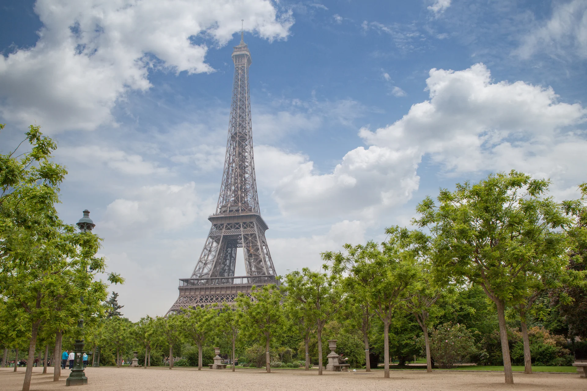 The Eiffel Tower rises beyond tree-lined paths near the Champ de Mars