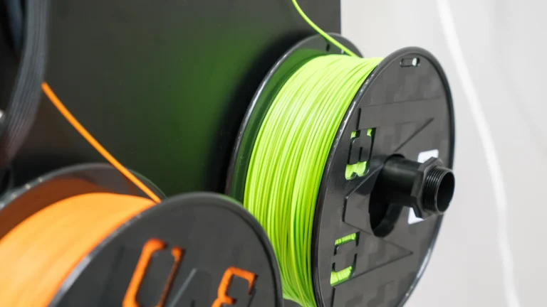 Two black spools hold bright green and orange 3D printer filament.